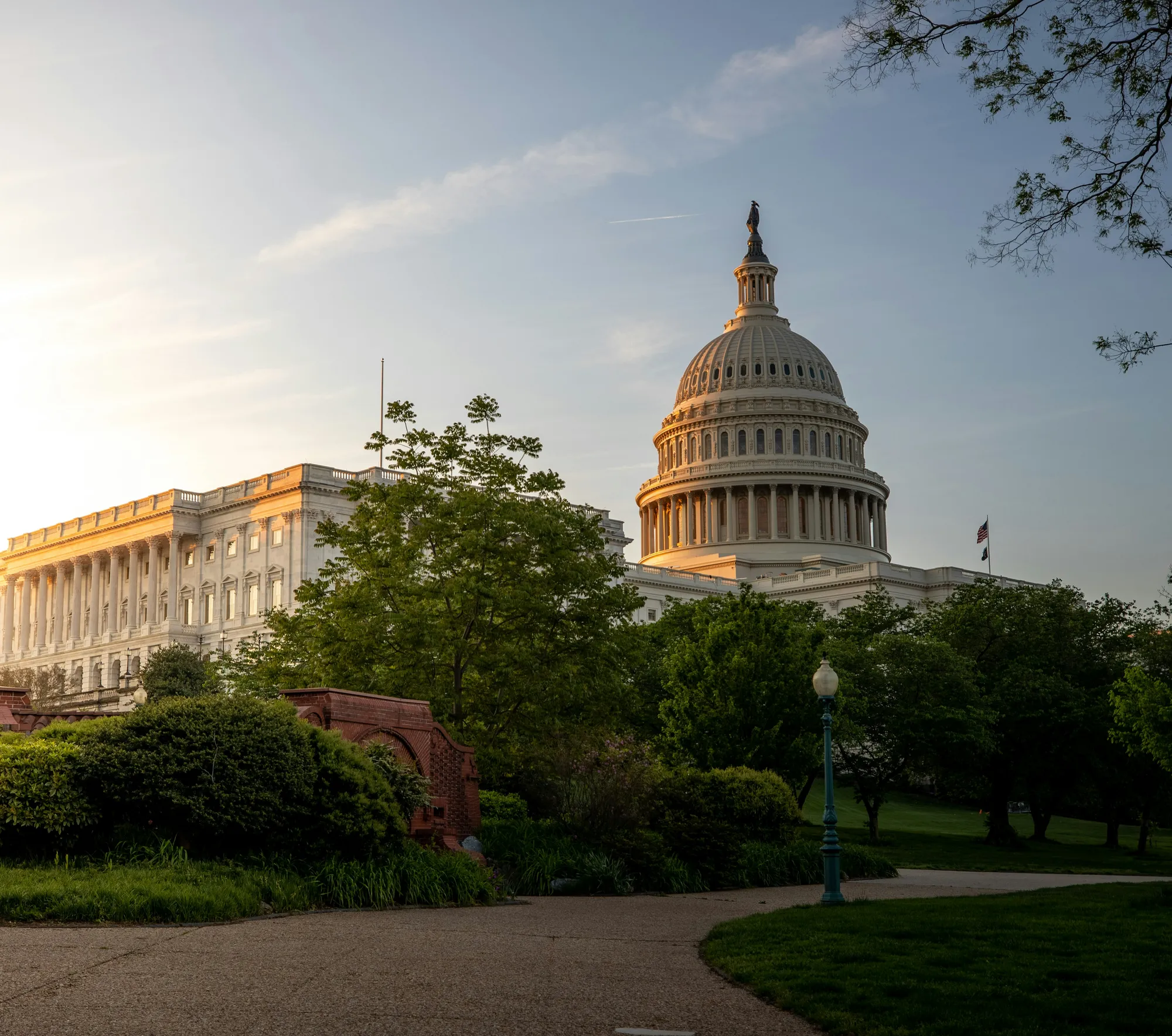 The dome and west front of the US Capitol in golden-hour light, seen from the grounds below