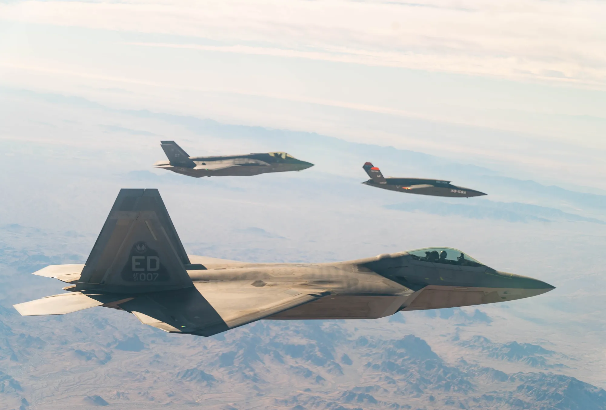 An F-22 Raptor leading an F-35A Lightning II and an XQ-58A Valkyrie drone in formation over the Yuma Proving Ground